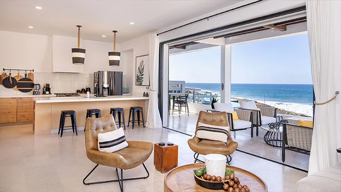 the cove at cerritos 102 living room -  Open-concept kitchen and living area at Residence 102 featuring leather lounge chairs, wood accents, and ocean views from the terrace.