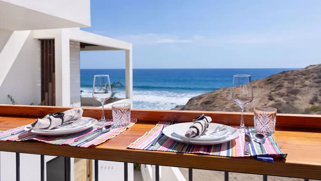 Residence 100 – Private Terrace with Ocean View -  Ocean-view terrace at Residence 100 with a two-person dining setup, featuring colorful placemats, crystal glasses, and neatly set plates overlooking the Pacific at The Cove at Cerritos.